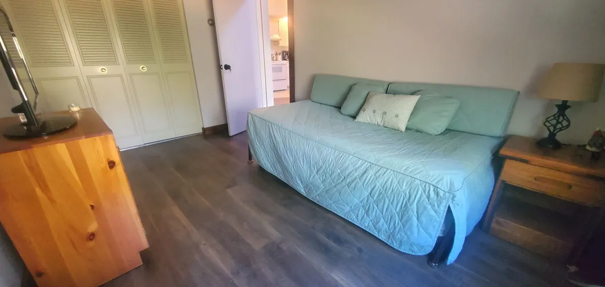A comfortable living area featuring a stylish sofa, nightstand, dresser, and closet, all arranged to create an inviting space for relaxing or gathering with friends. The decor is bright and the space feels open and social.