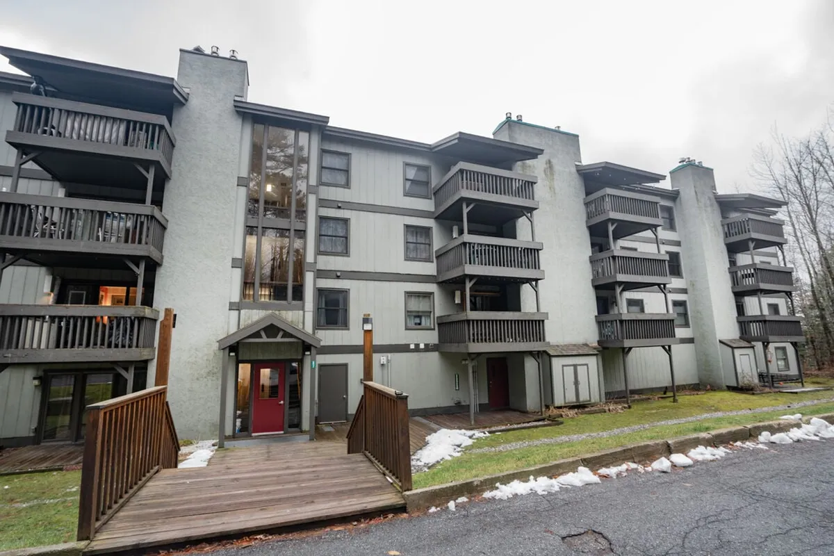 An exterior shot of the main entrance to the property, featuring balconies and attractive landscaping. The scene suggests easy access to communal amenities and invites guests to imagine summer relaxation or socializing outdoors.
