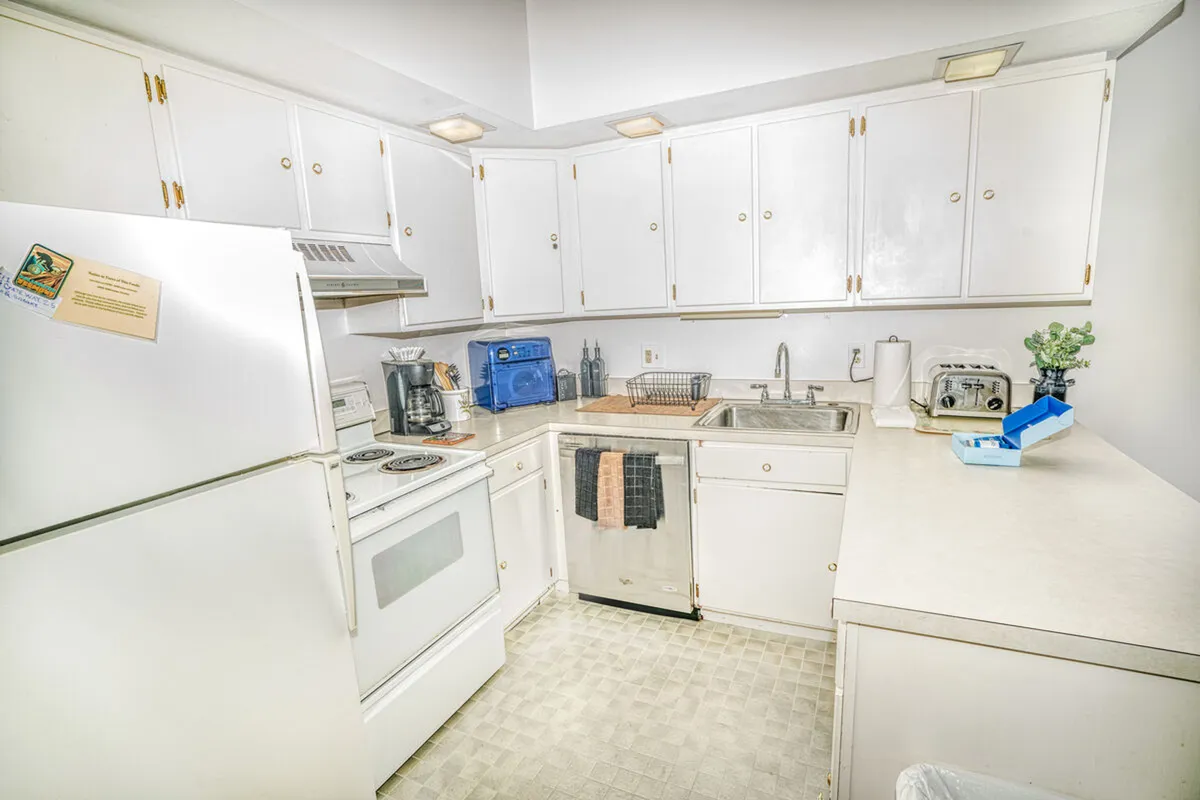 A cozy kitchen area featuring white cabinetry, a stainless steel sink, and essential kitchen appliances. The atmosphere is inviting, ideal for everything from baking cookies to enjoying morning coffee.