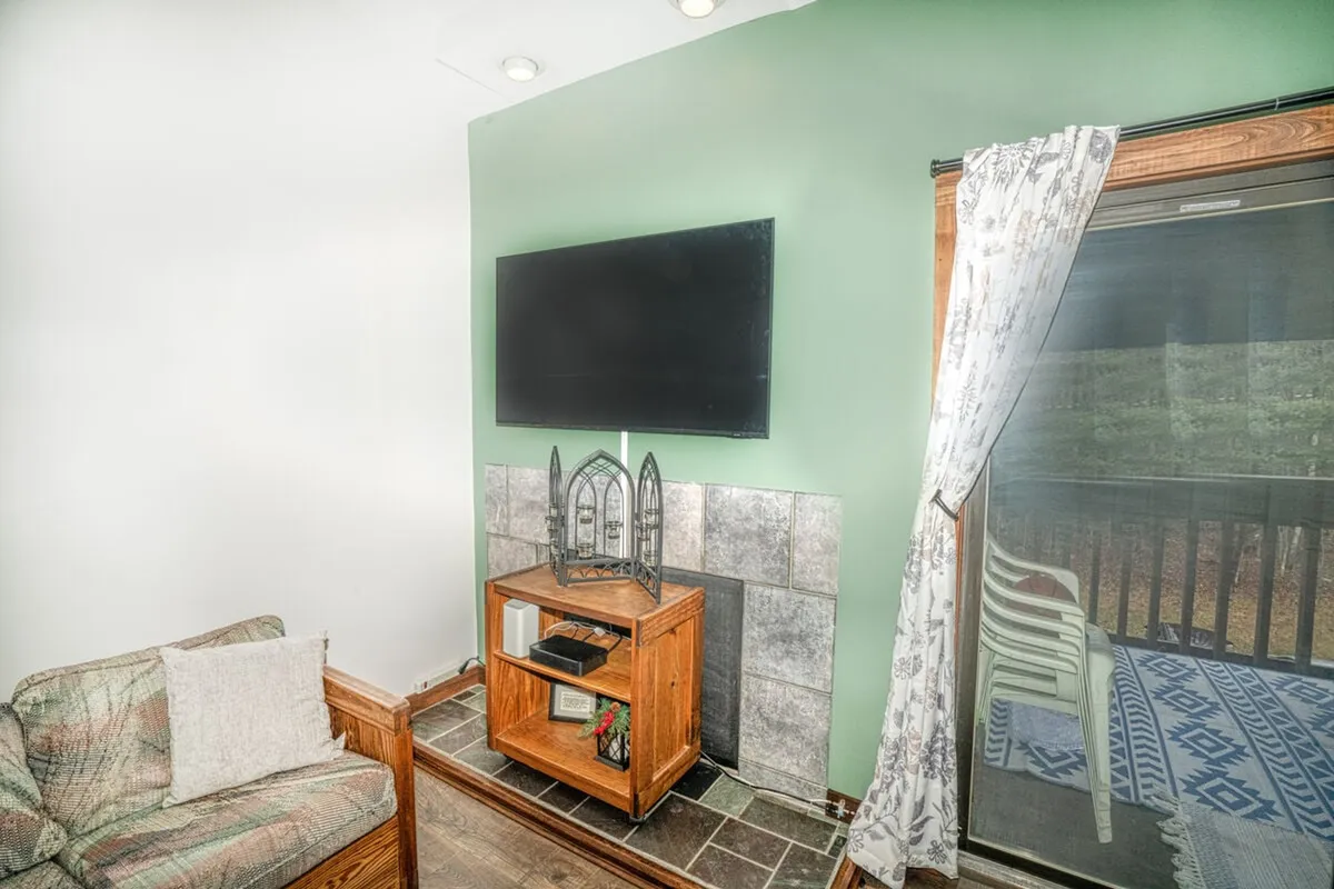 A bright and comfortable living area with a clear view of the television, a stylish wooden cabinet, a sofa, and a sliding door that appears to lead to a balcony. It visually connects the interior space to the outdoors.