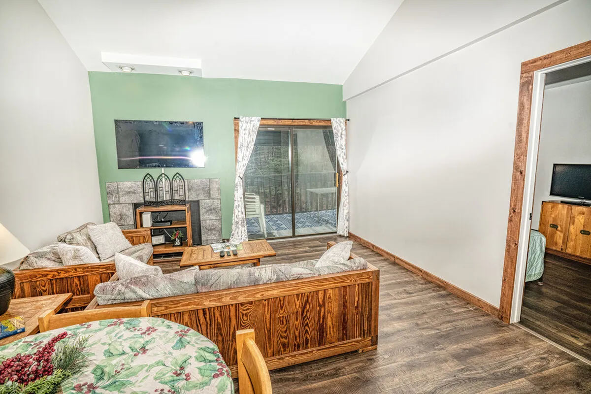 A warm, inviting living room featuring a plush sofa set, a cozy fireplace, a large flat-screen television, and soft curtains. The arrangement encourages relaxation, conversation, or enjoying a movie after a day outdoors.