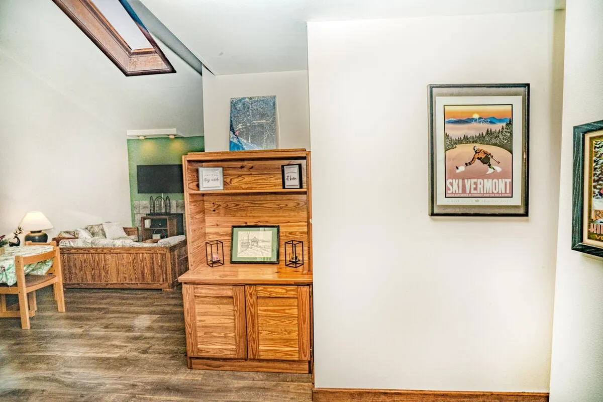 A cozy interior scene featuring a wooden storage cabinet and a 'Ski Vermont' poster on the wall. The setting is warm and inviting, evoking the atmosphere of a ski lodge and suggesting a storage or mudroom area ideal for winter gear.