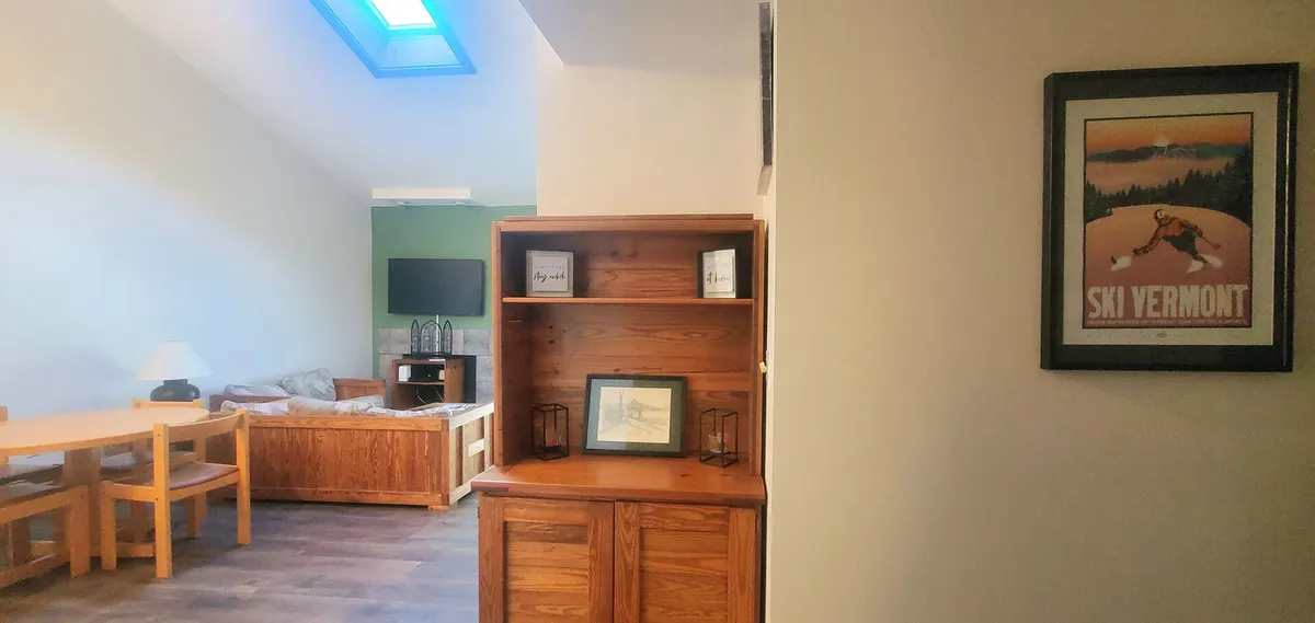 A welcoming living area with a wooden shelving unit, dining table, sofa, and a ski-themed poster. The space feels lived-in and suitable for relaxing after outdoor adventures, with hints of winter fun and group gatherings.