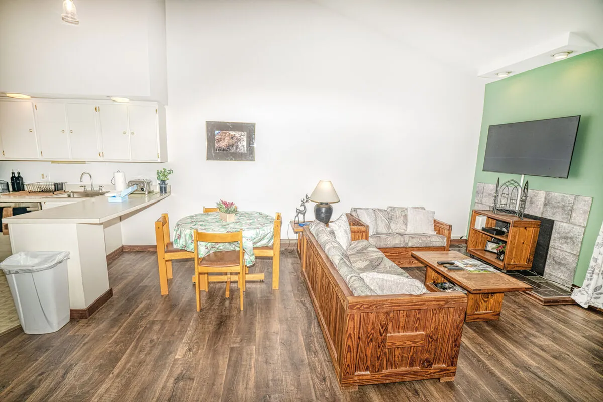 This inviting interior scene showcases a cozy living and dining area with warm wooden furniture, a dining table perfect for shared meals, and a television for relaxing movie nights. The ambiance is comfortable and welcoming, ideal for family gatherings or unwinding after a day of Vermont adventures.