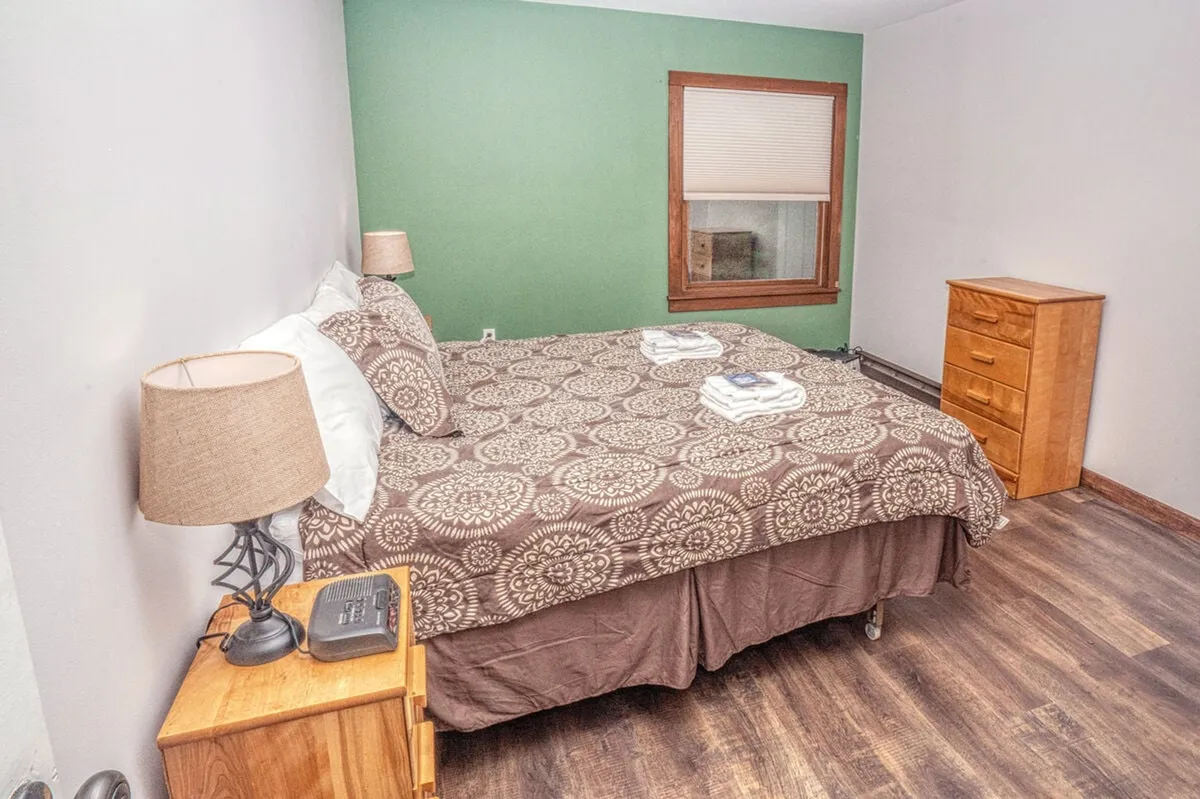 This image captures a cozy bedroom with a patterned bed, nightstands with lamps on either side, and a window letting in natural light. The soft bedding and gentle lighting create an inviting, restful atmosphere ideal for relaxation.