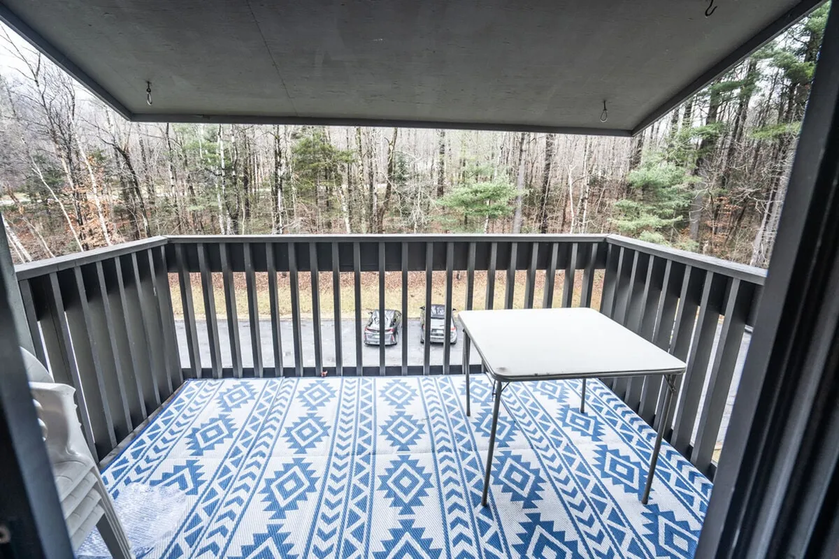 A peaceful outdoor balcony with a blue patterned rug, a table, and surrounding trees, offering a tranquil spot for morning coffee or relaxing amid nature.