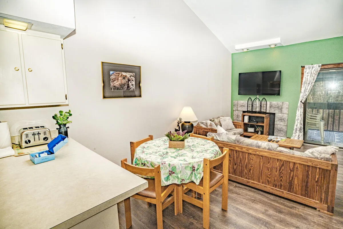 A cozy, welcoming living room featuring a comfortable sofa, a dining table with a floral tablecloth, a wall-mounted television, and decorative wall art—an inviting spot to unwind after a day on the slopes.