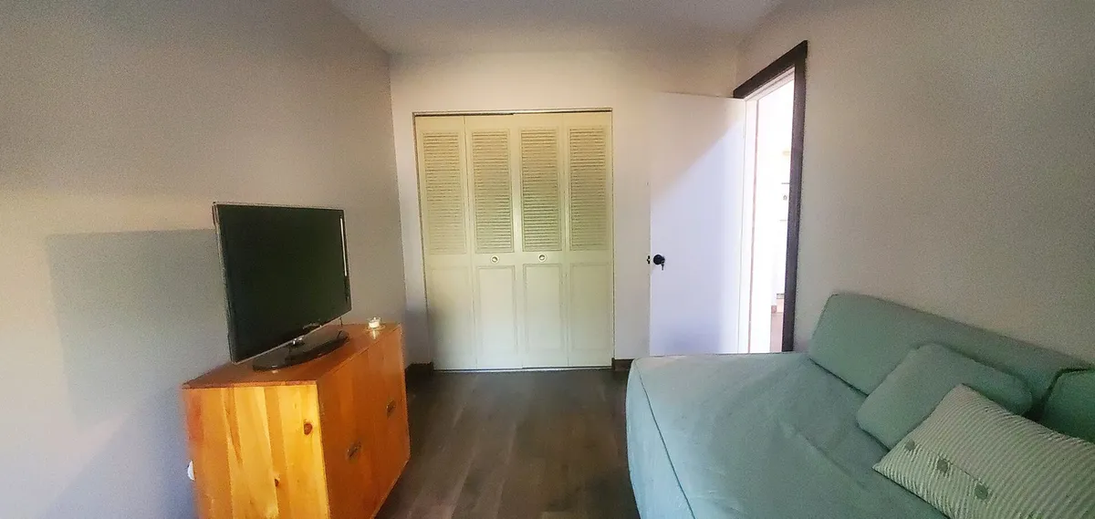 This image presents a welcoming living room with a comfortable sofa, large flat-screen TV, and wooden cabinet. The space exudes an inviting atmosphere, ideal for relaxing, watching movies, or spending time together after a day outdoors. The inclusion of closet doors and a well-organized layout adds to the sense of comfort and homeliness.